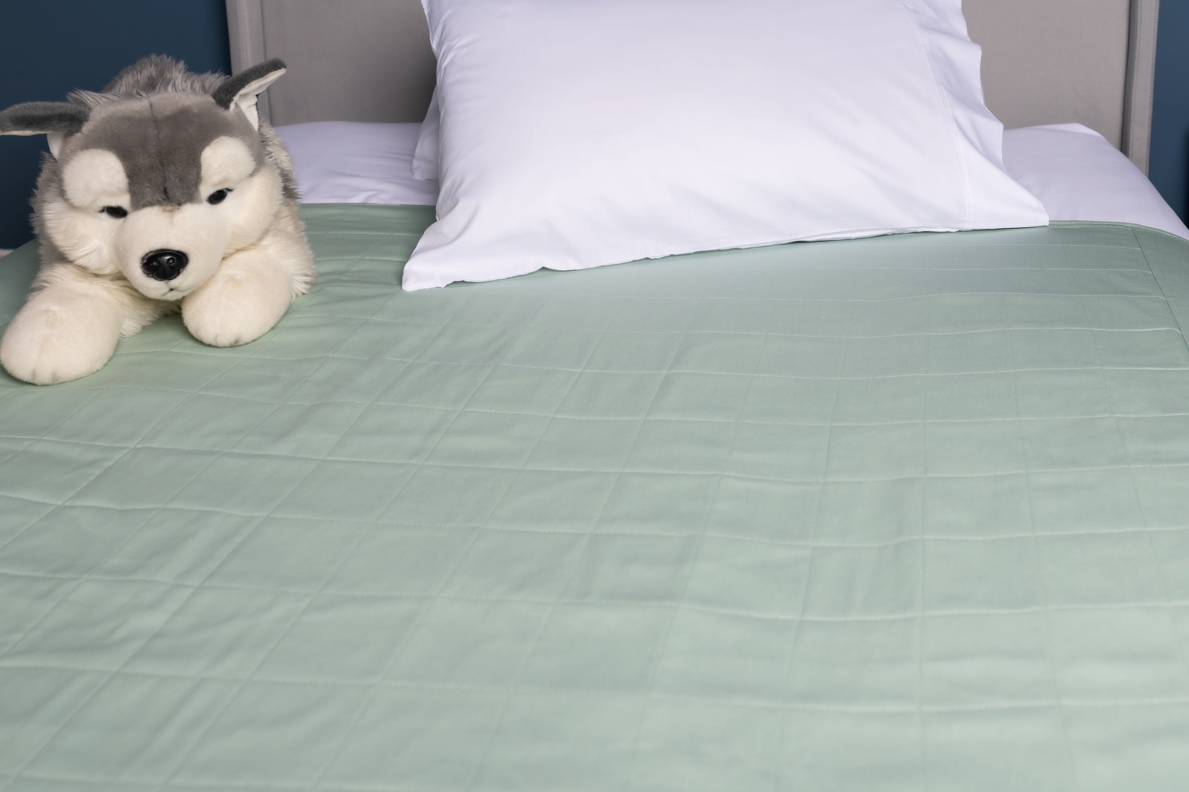 Evelyn & Co grey organic bed wetting pad with tuck-in wings laid flat on a bed