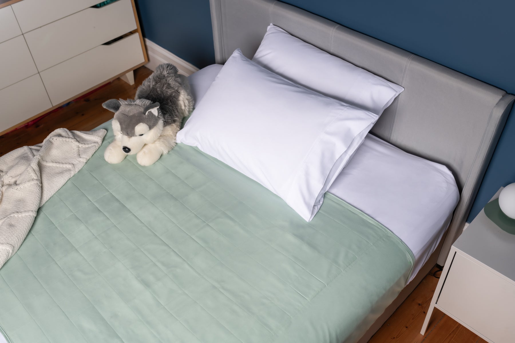 Evelyn & Co sage green organic bed wetting pad with tuck-in wings laid flat on a bed